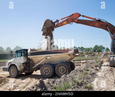 Grande dumper articolato grigio in cantiere durante il carico e il trasporto del terreno. Preparazione del cantiere, lavori di terra Foto Stock