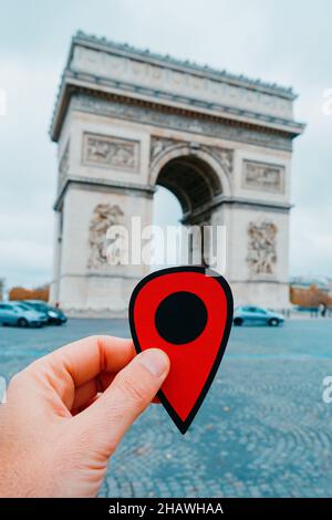 La mano di un giovane caucasico che tiene un marcatore rosso che punta il famoso Arc de Triomph a Parigi, Francia Foto Stock