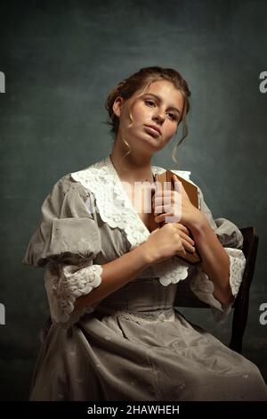 Ritratto vintage di giovane bella ragazza in abito grigio di stile medievale isolato su sfondo scuro. Confronto del concetto di eas, stile fiammingo. Foto Stock