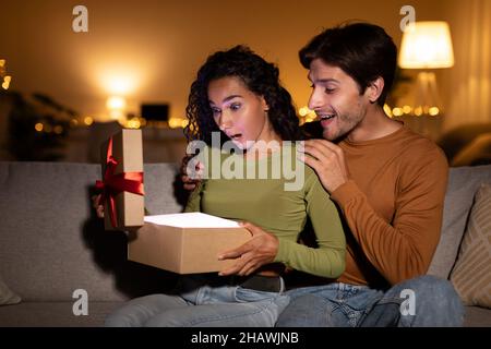 Fidanzata sorprendente ragazza con regalo, lei apertura Box a casa Foto Stock