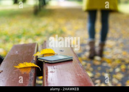 Smartphone dimenticato su una panca da parco. La donna sta lasciando da una panca dove ha perso il suo telefono cellulare. Foto Stock