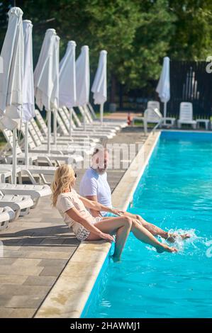 Coppia matura che gode di bel tempo vicino alla piscina Foto Stock