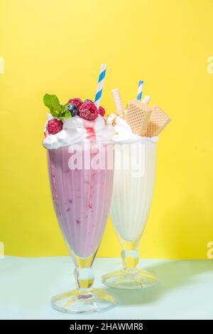 Bevande rinfrescanti estive, frullati, frullati pazzi con gelato, frutti di bosco, vaniglia, cioccolato. Su uno sfondo giallo blu brillante Foto Stock