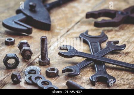 Strumenti di lavoro vintage. Vecchia chiave in metallo, pinze e chiave regolabile su tavola in legno. Vite arrugginita, bullone e dado di fissaggio in officina. Industriale Foto Stock