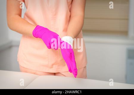 Mano di estetista mette su guanti rosa sterili si prepara a ricevere i clienti al chiuso Foto Stock