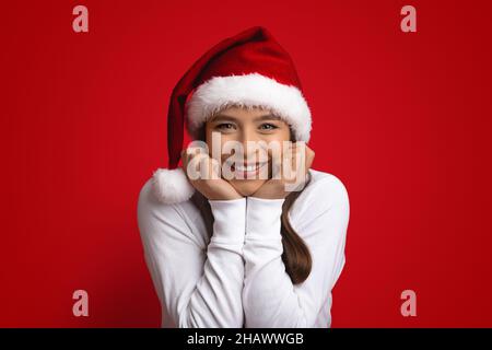 Ritratto di bella giovane donna che indossa Santa Hat toccare il volto in eccitazione Foto Stock