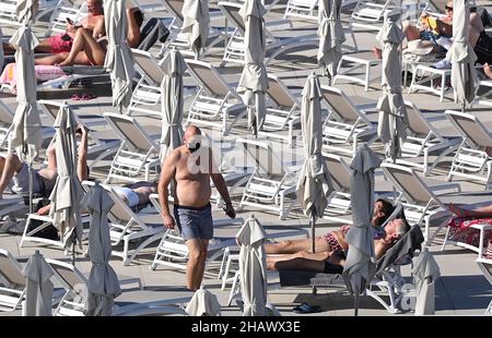 I vacanzieri che indossano maschere protettive per proteggere contro Covid-19 sono visti dai lettini di un hotel a Tenerife, Spagna. Dicembre 2021. Foto Stock