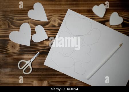 Cuori fai da te scolpiti a mano in carta da copia bianca. Preparazione per l'artigianato per San Valentino. Idee regalo per San Valentino, amore giorno, concetto di febbraio Foto Stock
