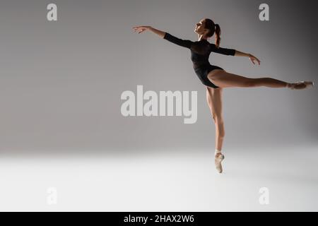 donna per tutta la lunghezza in scarpe ballerine danzanti con le mani distese su grigio scuro Foto Stock