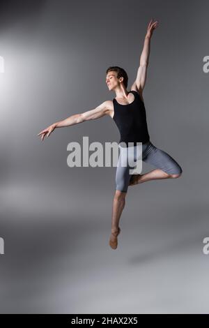 giovane e aggraziato ballerino gesturing mentre levitating su grigio scuro Foto Stock