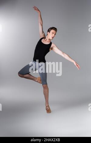 giovane e grazioso uomo gesturing mentre esegue balletto danza in grigio scuro Foto Stock