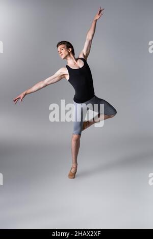 giovane ballerina aggraziata che gesturisce mentre si esibisce balletto in grigio scuro Foto Stock