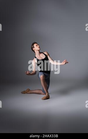 ballerina elegante a tutta lunghezza in piedi sul ginocchio, mentre si esegue balletto in grigio scuro Foto Stock