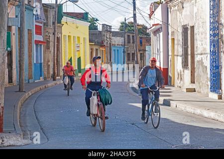 Uomini cubani che cavalcano in bicicletta attraverso la strada colorata nel centro storico della città Camagüey sull'isola Cuba, Caraibi Foto Stock