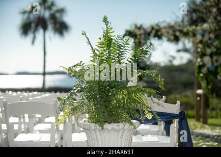 Sedie bianche per cerimonie di nozze in isola decorate con archi e nastri blu Foto Stock