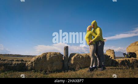 Uomo e donna in abbigliamento sportivo giallo verde. Una coppia incantevole di viaggiatori si abbraccia e bacia vicino alla pietra vecchia godendo il paesaggio delle Highland. Due viaggiatori sono Walkin Foto Stock