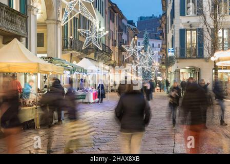 Mercatino di Natale al crepuscolo, folla di persone sulla strada di una città con le luci di natale. Centro storico di Varese, corso Matteotti Foto Stock