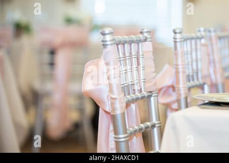 Sedie chiavari dorate con archi rosa e nastri alla cerimonia di nozze del country club Foto Stock