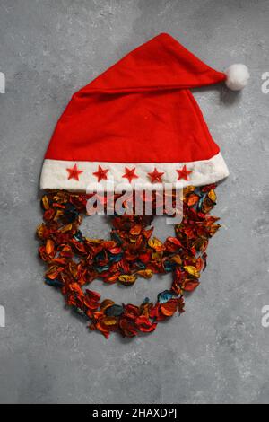 Cranio umano in profilo in berretto rosso Babbo Natale con finiture bianche e pompon. Isolato su sfondo di pietra. Foto Stock