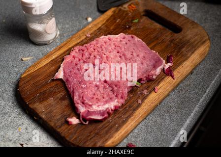 Un pezzo martellato di carne di maiale cruda su un tagliere Foto Stock