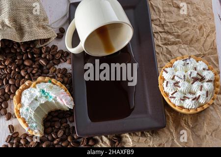 Mini torta di ganache al cioccolato bianco con un boccone, accanto a una tazza di caffè capovolta su carta marrone. Foto Stock