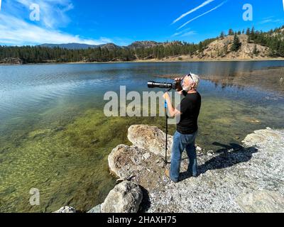 Uomo in piedi al bordo del lago di scattare una foto, Okanagan, British Columbia, Canada Foto Stock