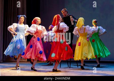 Omsk, Russia. 05 dicembre 2021. Le ballerine di Prohodka che indossano foulard nazionali ballano sotto forma di un rombante intorno al bayan giocatore. P Foto Stock
