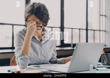 Signora di affari overworking che soffre di mal di testa mentre lavora a distanza da casa Foto Stock