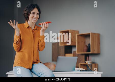 Felice dipendente ispanico che utilizza il vivavoce o un assistente vocale virtuale sul telefono cellulare Foto Stock