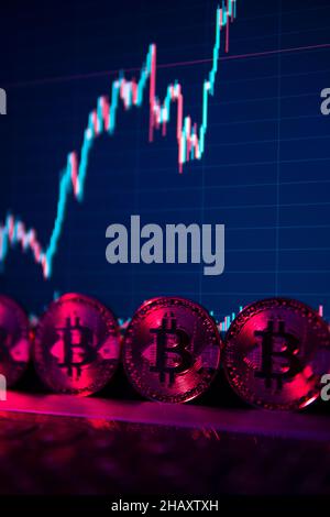 Le monete Bitcoin sono in piedi sul laptop in neon Light con una carta su uno schermo sullo sfondo Foto Stock