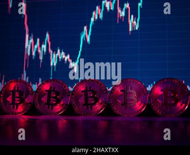 Le monete Bitcoin sono in piedi sul laptop in neon Light con una carta su uno schermo sullo sfondo Foto Stock