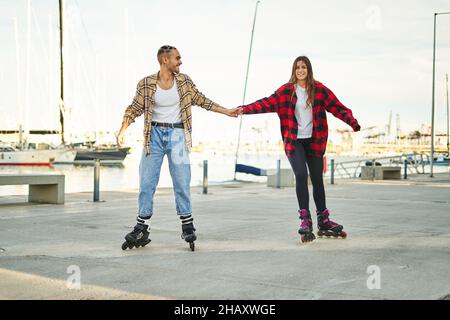 Un corpo pieno di giovani amici positivi che tengono le mani sui pattini a rotelle godendo del tempo libero piacevole insieme sul lungomare al tramonto Foto Stock