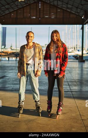Un corpo pieno di giovani amici positivi sui pattini a rotelle godendo di un piacevole tempo libero insieme in piedi sul lungomare al tramonto Foto Stock