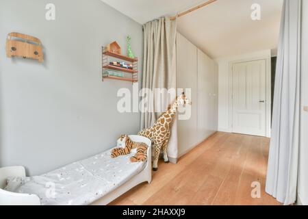 Interno di luce moderna camera da letto per bambini con pareti bianche arredate con comodo letto e diviso con tende e decorate con giocattoli e scaffali Foto Stock