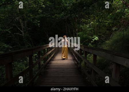 Vista posteriore di una donna irriconoscibile che cammina su un ponte pedonale di legno sul fiume Mao in Galicia Sacra in Spagna Foto Stock