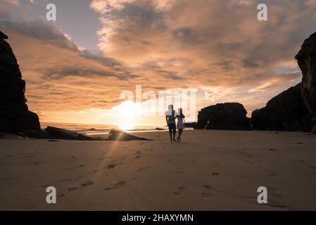 Silhouette di uomo che abbraccia la ragazza mentre si trova sulla spiaggia di sabbia delle cattedrali vicino alla montagna e ammirando il cielo del tramonto insieme Foto Stock