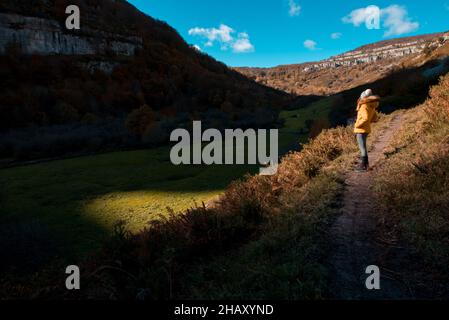 Anonimo femmina turista in abiti caldi in piedi sul sentiero in prato erboso vicino montagne in giornata di sole in Cantabria Foto Stock