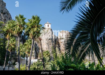 La torre di Shabby si trova sulla cima di una montagna rocciosa nella natura di Guadalest con alte palme nella soleggiata giornata estiva Foto Stock