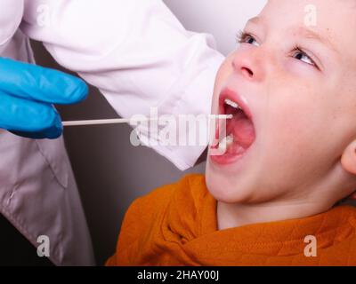 Specialista medico irriconoscibile in guanto di lattice prendendo il campione di saliva dalla bocca di un piccolo paziente mentre fa il test del coronavirus contro backgroun grigio Foto Stock