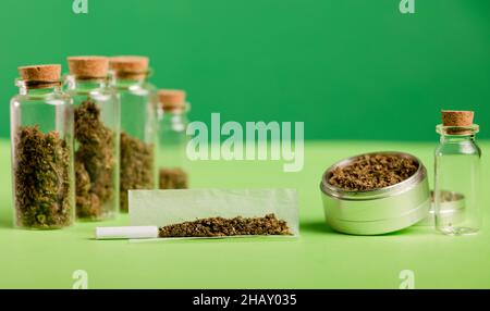 marijuana tritata, su carta di sigaretta con filtro e vasi di vetro ermetici con diversi tipi di cannabis su legno, con macinacaffè. Foto Stock