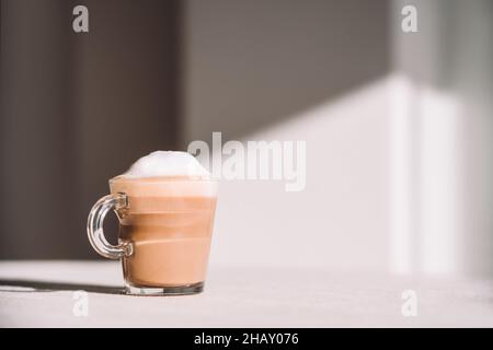 Bicchiere di latte macchiato schiumoso servito a tavola in giornata di sole in cucina Foto Stock