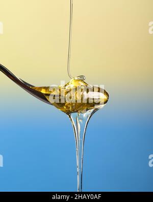 Ruscello di miele limpido versando su un cucchiaino e traboccante, isolato, su uno sfondo bianco blu e giallo Foto Stock