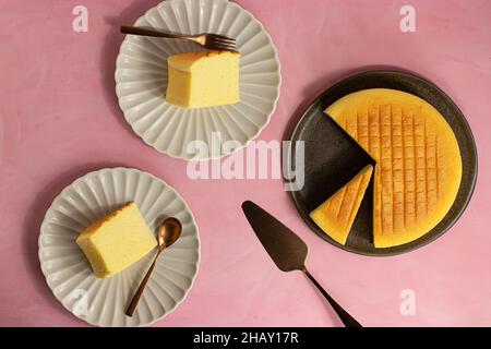 Vista dall'alto della deliziosa cheesecake di cotone servita su piatti vicino alla spatola su sfondo rosa Foto Stock