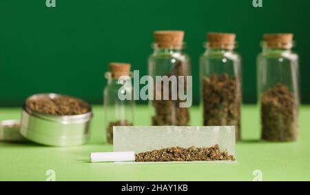 marijuana tritata, su carta di sigaretta con filtro e vasi di vetro ermetici con diversi tipi di cannabis su legno, con macinacaffè. Foto Stock