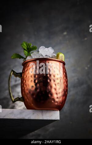 Cocktail mulo di Mosca servito in tazza di ghiaccio e fetta di lime in un angolo del tavolo su sfondo grigio Foto Stock