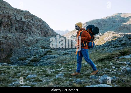 Vista laterale del viaggiatore con zaino a piedi su terreni erbosi con sentieri e pietre durante il viaggio nella natura Foto Stock