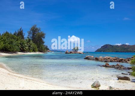 Costa rocciosa con piccola baia e isola Anse Takamaka Praslin Island Seychelles Foto Stock