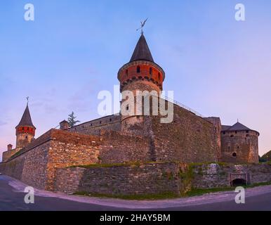Il panorama serale panoramico dello storico castello di Kamianets-Podilskyi in pietra con alte torri e massicci bastioni in una luce oscurato al tramonto, Ucraina Foto Stock