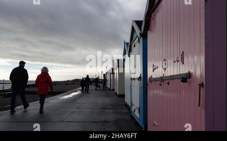 Felixstowe, Suffolk, UK : la gente cammina lungo il lungomare di Felixstowe in un inverno freddo e noioso passato una linea di capanne di spiaggia di fronte al mare. Foto Stock