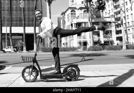 uomo felice uomo d'affari che guida elettro scooter su sfondo urbano, noleggio di trasporto. Foto Stock